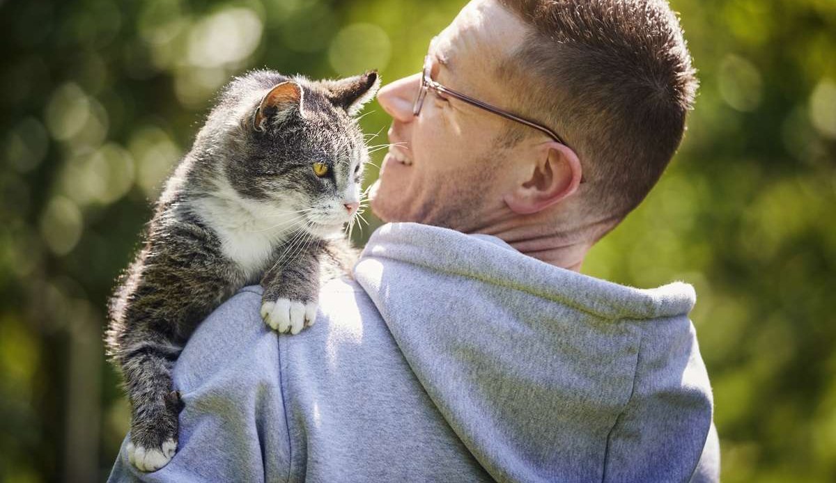 Усміхнений чоловік несе свого старшого смугастого кота в саду